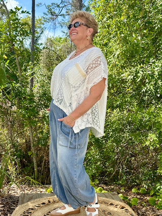White lace handkerchief hem top with short sleeves and sheer detailing worn with light wash jeans.
