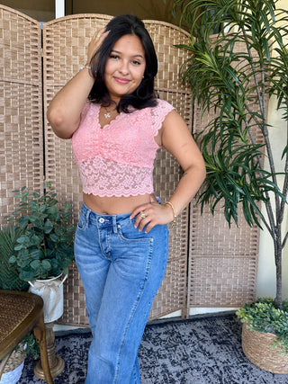 Pink lace crop top with scalloped trim and cap sleeves styled with blue jeans.
