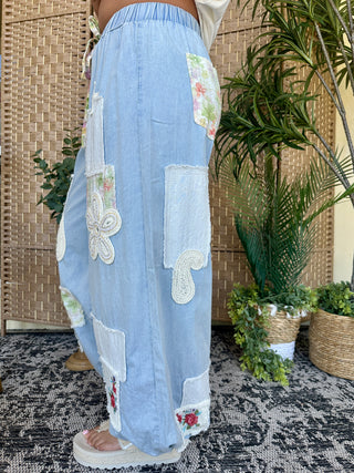 Light blue denim joggers with white lace patches and floral embroidered details throughout.
