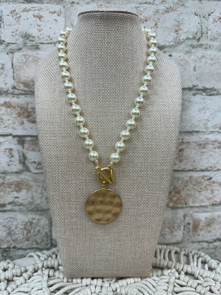 Cream pearl beaded necklace with gold hammered disc pendant on display bust.

