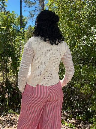 Ivory cable knit vest with mauve striped sleeves and tie detail, worn back view with pink ribbed pants.
