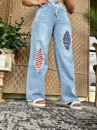 Light blue distressed jeans with red striped and navy polka dot patches on thighs, wide leg cut.
