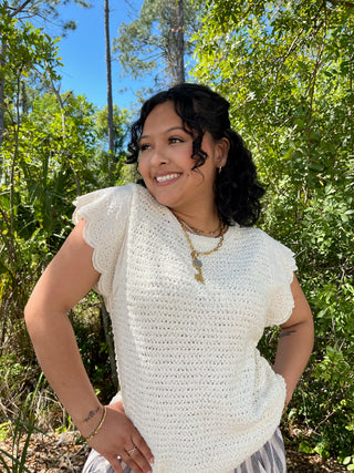 Cream textured short-sleeve top with eyelet ruffle sleeves and openwork knit pattern.
