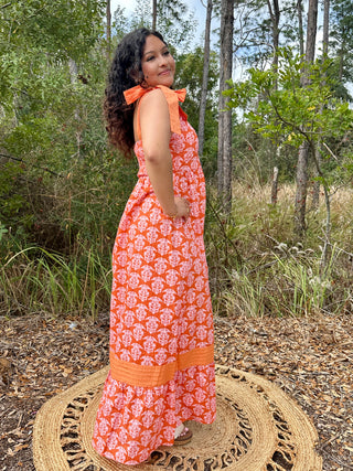 Orange maxi dress with white damask print, ruffled neckline, and contrasting orange trim band.
