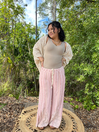 Pink wide-leg pants with textured weave, paired with cream tank top and open knit cardigan.
