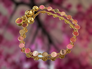 Gold bracelet with pink tourmaline beads, gold spacers, and magnetic closure clasp against floral background.
