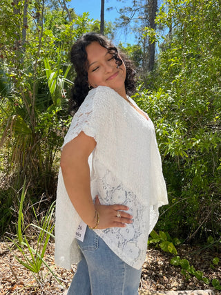 White lace short-sleeve top with handkerchief hem paired with denim jeans.
