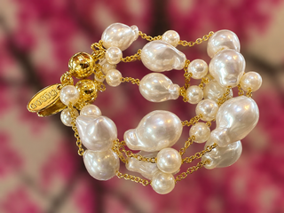 Gold chain bracelet with white baroque pearls and golden filigree bead accents on pink background.
