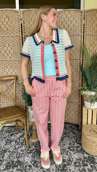Cream knit cardigan with blue and red striped trim, red button front, worn with light blue tank and red gingham pants.
