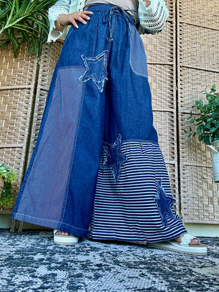 Blue denim wide-leg pants with star and stripe patchwork design, drawstring waist, relaxed fit.
