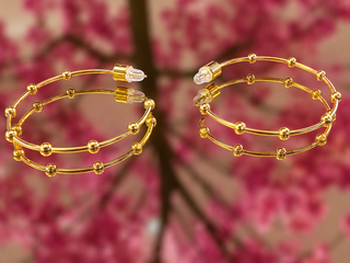 Gold bead accent hoop earrings with crystal studs displayed against pink floral background.
