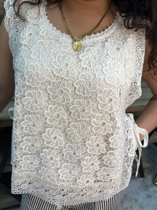 Cream lace crochet sleeveless top with intricate floral pattern and decorative pearl button details.
