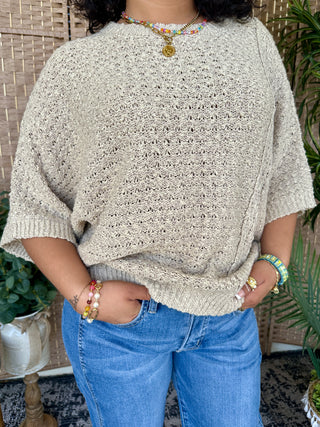 Taupe knit sweater with asymmetrical hem and open stitch pattern, short sleeves, crew neckline.
