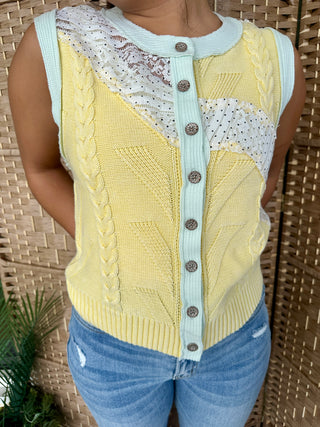 Lemon yellow sleeveless sweater vest with cable knit pattern, light blue trim, metallic buttons, and patterned color-block pa
