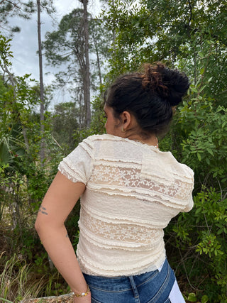Cream lace short-sleeve top with textured stripes and sheer lace panels, worn with blue jeans.
