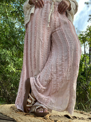 Blush pink wide-leg pants with vertical textured stripes and decorative lace detailing throughout.
