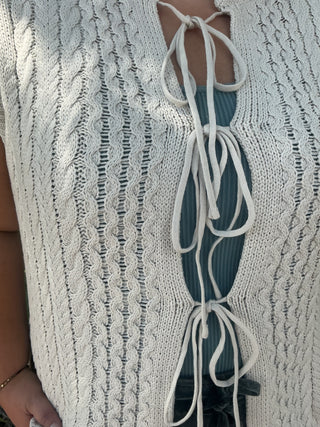 Bone cable knit sweater vest with a tie front detail, perfect for layering or standalone wear.