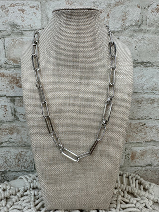 Silver elongated link chain necklace displayed on beige linen bust form.
