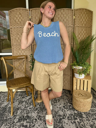 Blue ribbed sleeveless tank top with "Beach" text graphic paired with khaki shorts.
