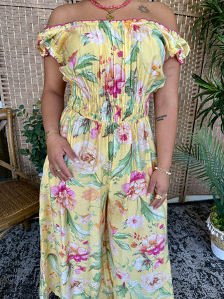 Yellow off-shoulder jumpsuit with pink and red floral print, ruched waist, short puffed sleeves.
