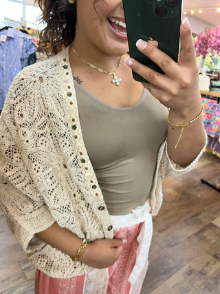 Cream crochet shrug with button details worn over gray fitted top.
