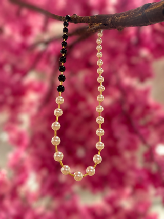 Black and white pearl beaded necklace with gold-toned chain against pink floral background.

