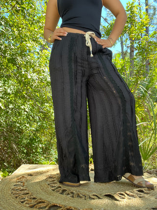 Black wide-leg pants with textured vertical stripes and cream drawstring waist.
