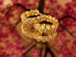 Gold round huggie hoop earrings with bezel-set crystals and textured metalwork, displayed on pink floral background.
