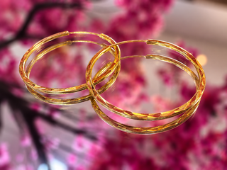 Gold twisted hoop earrings displayed against pink floral background.
