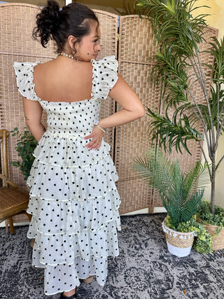 White tiered ruffle dress with black polka dots and puff sleeves, open back design.
