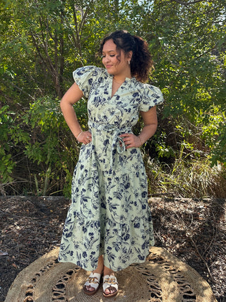 Sage green midi dress with navy floral print and short ruffled sleeves, worn with sandals.
