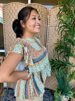 Turquoise floral print top with colorful ruffled sleeves and navy trim detail.
