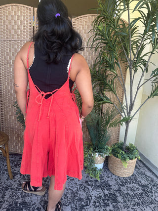 Bright red denim romper with lace-up back detail and adjustable straps, knee-length cut.
