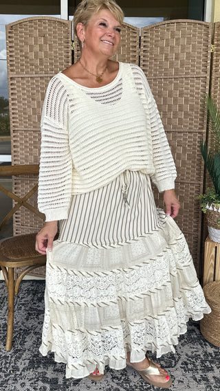 Ivory slouchy sweater with open knit pattern and long sleeves paired with layered striped skirt.
