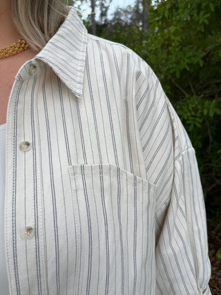 Ivory button-down shirt with black vertical stripes, featuring a collar and chest pocket.
