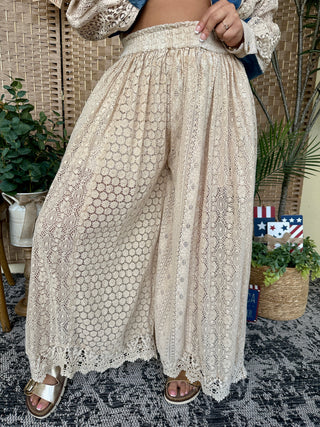 Cream lace wide-leg pants with geometric and floral patterns, elastic waist, shown on model outdoors.
