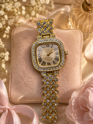 Gold square watch with crystal-embellished bezel and band, roman numeral face on blush velvet display.

