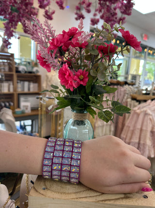 Magenta stretch bracelet with iridescent square crystals worn on wrist.

