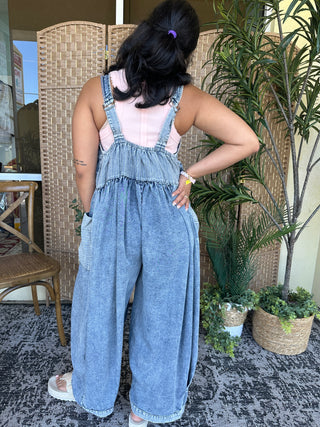 Light blue denim jumpsuit with wide legs, adjustable straps, and oversized fit shown from back view.
