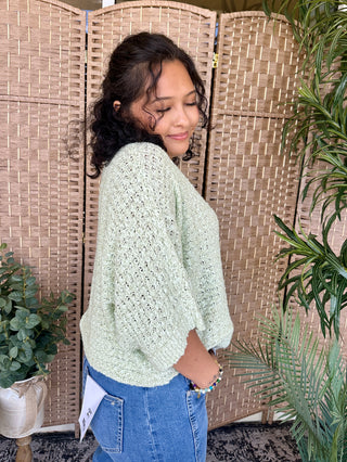 Pale green asymmetrical knit sweater with textured weave and draped side detail.
