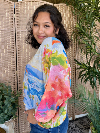 Colorful harbor print batwing top with blue, pink, yellow and green floral design on white knit fabric.
