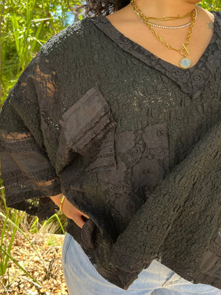 Black lace top with handkerchief hem and short sleeves, layered over white pants.
