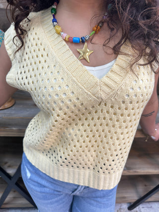 Cream open knit sweater vest with textured pattern and colorful beaded star necklace.
