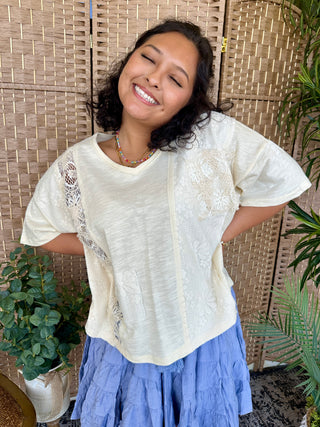 Cream short-sleeve top with mixed lace and textured patchwork panels on natural linen fabric.
