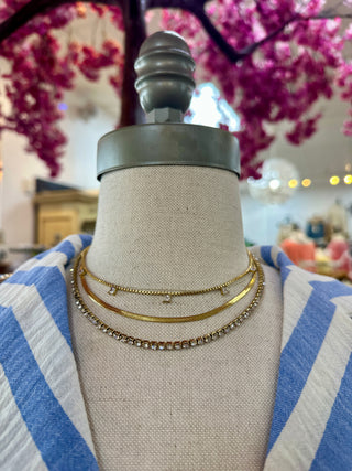 Layered gold tennis necklaces displayed on cream mannequin wearing blue and white striped garment.
