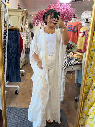 Cream textured kimono with long sleeves worn open over white tank and pants in boutique dressing room.
