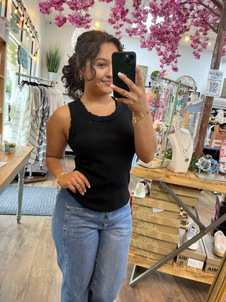 Black ribbed knit tank top with scalloped neckline worn with blue jeans.
