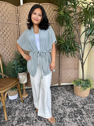 Seafoam open weave short-sleeve cardigan with tie waist worn over white pants.
