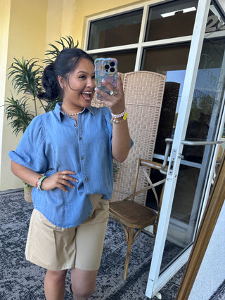 Light blue chambray button-up shirt with rolled sleeves, paired with cream-colored shorts.
