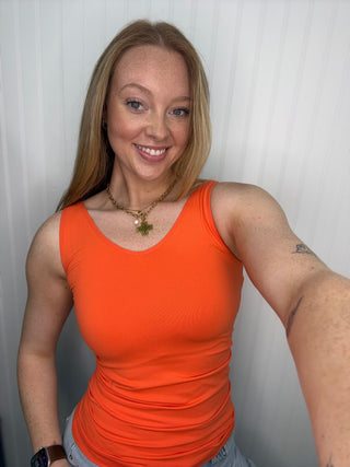 Orange sleeveless tank top with ruched sides, shown on model wearing gold chain necklace.
